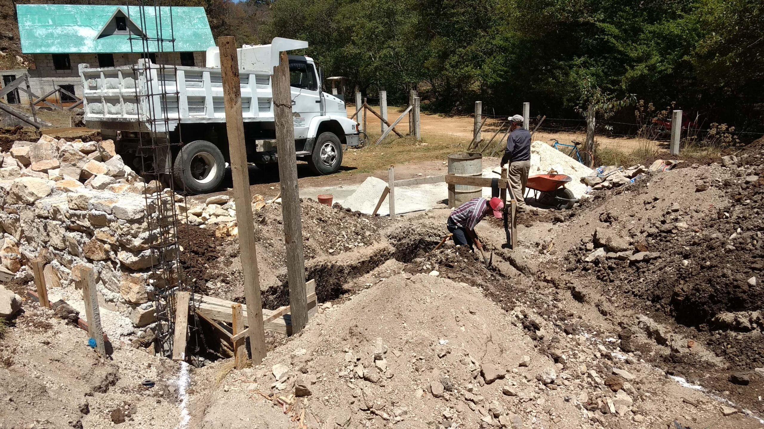 Workers hand-digging foundation trenches with rebar columns and a materials truck on a self-built house site near San Cristóbal de las Casas, Chiapas